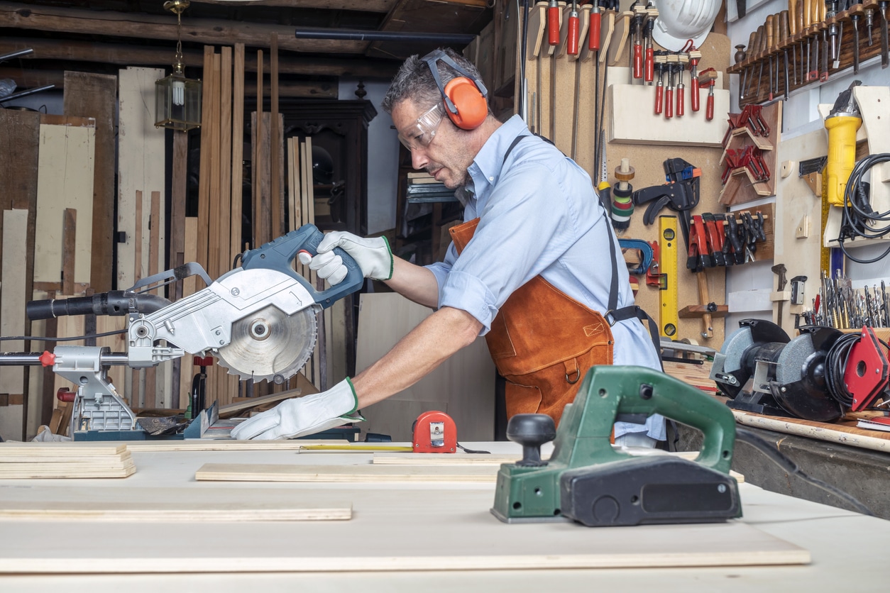 Man wearing earmuffs using a rotary saw in his woodshop. 