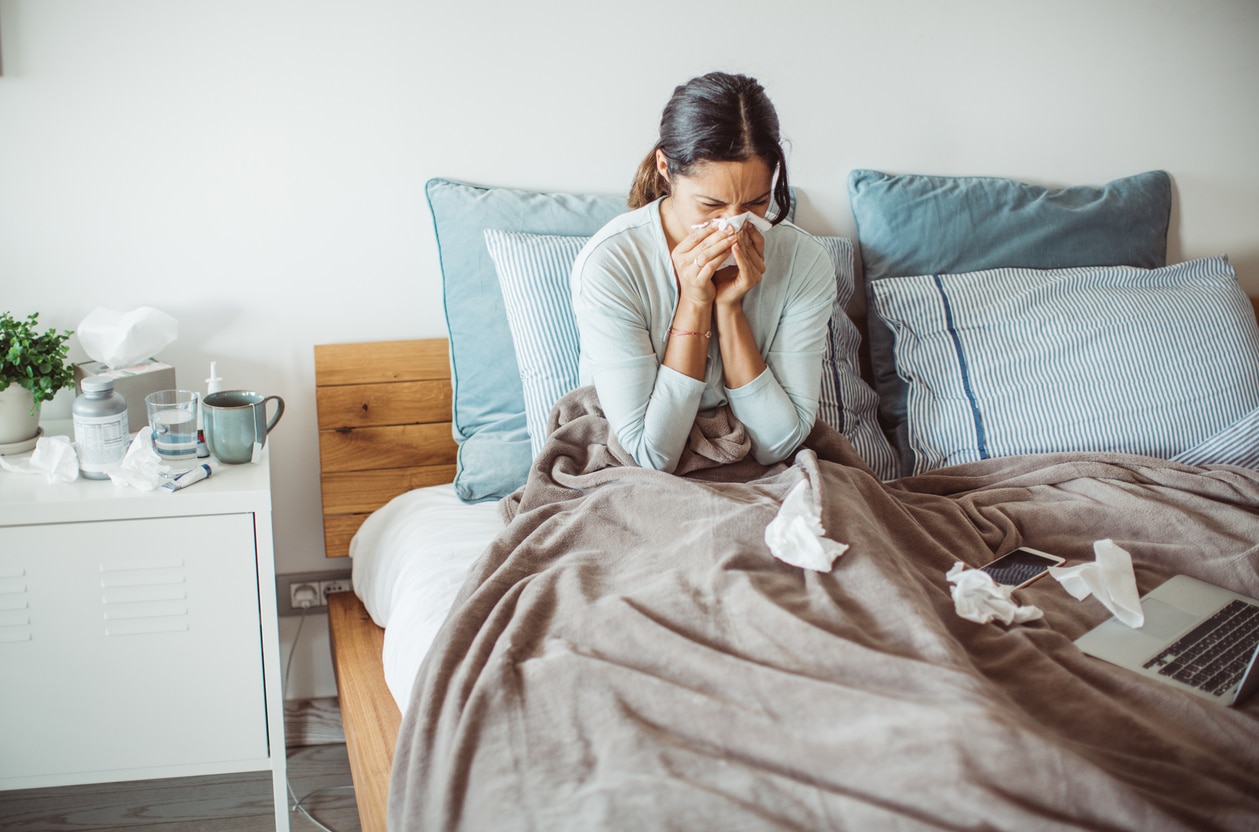 Sick woman blowing her nose in bed.