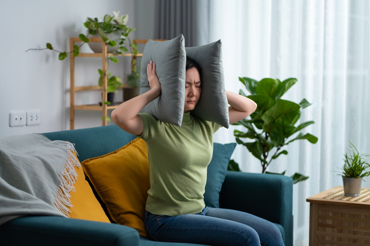 Woman putting pillows around her ears to drown out music ear