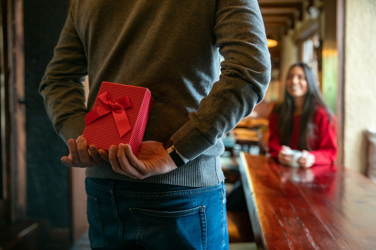 Man surprising woman with a gift while celebrating Valentines at a restaurant.